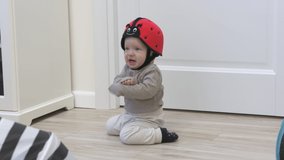 Cute baby boy wearing soft safety helmet discovering new things at home, 7 month old infant on the floor playing, learning to walk, craw sit and stand. High quality 4k footage