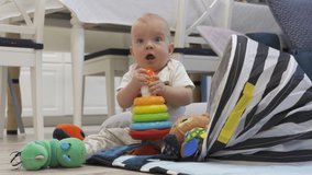 Baby sitting on the floor playing with toys from toy storage basket, cute 7 month old baby boy having fun exploring new world around him at home. High quality 4k footage