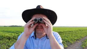 A guy in a hat looks through black binoculars in the park