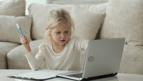 Little girl using a laptop computer, studying through an online e-learning system while sitting in the living room