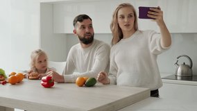 Happy family live, a pregnant woman shoots a video blog on a smartphone with her husband and little daughter in the kitchen