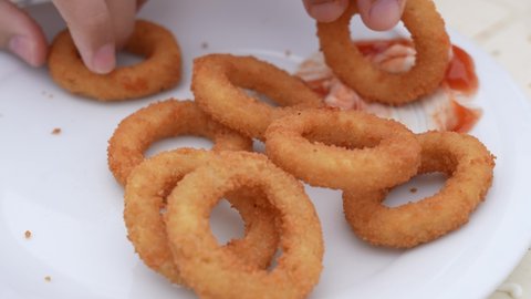 Close-up view 4k stock video footage of hands of father and young son eating tasty mouthwatering hot fresh just cooked crispy onion rings isolated on white plate background deeping snacks into sauce