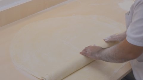 an arab baker pastry chef sprinkles corn starch with his hand on the rolled dough on the table. Man baker prepares puff pastry for baklava. Ramadan is approaching. Top view