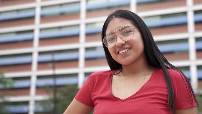 Portrait of carefree Hispanic Latin American Young Woman smiling in the city. Modern Female student girl from Andean Ethnicity (Ecuador, Peru or Bolivia) | Shutterstock HD Video #1081920359