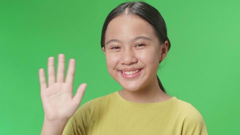 The Happy Young Asian Kid Girl Waving Hand And Say Bye Bye While Standing On Green Screen In The Studio
