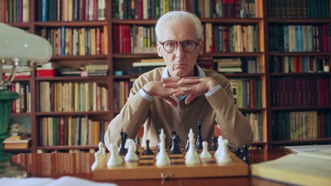 Concentrated senior male with crossed hands sitting at chess board in library