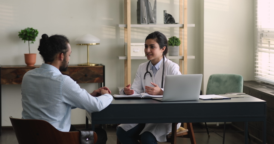 Happy millennial indian ethnicity female doctor sharing positive treatments results with african multiracial male patient at meeting in modern clinic office, regular checkup healthcare concept. Royalty-Free Stock Footage #1081924553