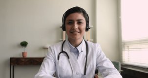 Web camera view skilled millennial generation indian ethnicity female general practitioner doctore in headphones with mic holding distant video call meeting with patients, modern tech telemedicine.