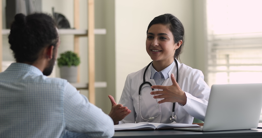 Skilled beautiful young indian female family doctor therapist general practitioner in white coat consulting african american male patient at checkup meeting in clinic, giving healthcare advices. Royalty-Free Stock Footage #1081924820