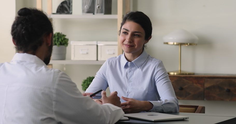 Smiling beautiful young indian ethnicity female patient discussing illness treatment with professional male african american doctor therapist at checkup meeting, sitting together at table in clinic. Royalty-Free Stock Footage #1081924826