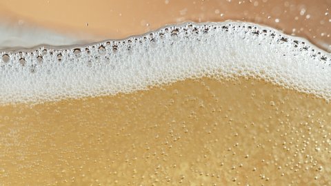 Super slow motion of champagne bubbles and foam texture. Isolated on golden background. Filmed on high speed cinema camera, 1000 fps
