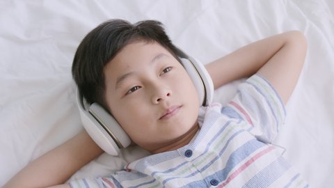 Top view of Asian male listening to music with headphones while lying in the bedroom at home morning