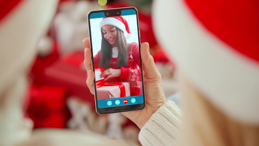 Happy senior grandparents couple in santa hats greeting grandchild opening Christmas gift on family cell phone video call, online virtual party meeting videocall on smartphone at home. Over shoulder | Shutterstock HD Video #1081956737