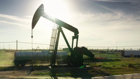 Oil pump jack with green landscape on rural countryside background. Fuel industry Equipment, global warming concept. Working oil pump at sunset sky. Pump Jack Extracting Crude Oil from Well, USA 4K