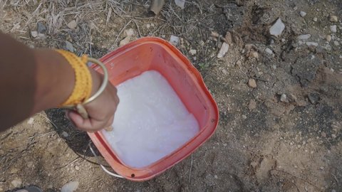Top view close-up shot of a South Asian man or male Farmer preparing chemical pesticide or fertilizer by mixing it well into a container filled with water during daytime.