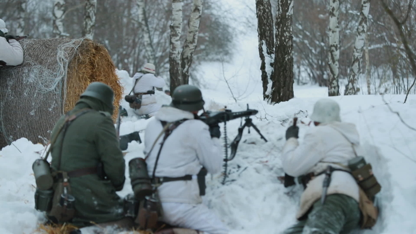 Men Dressed As German Wehrmacht Infantry Soldiers In World War II Hidden Sitting With Weapon In An Ambush And Aiming a Machine Gun at Enemy From Trench In Winter Day. Slow Motion.