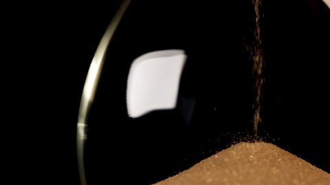 Hourglass. Sands move through hour glass. Sandglass close-up on a black background. Slow motion video. A pile of Golden sand at the bottom of the hourglass, small grains of sand fall from above.