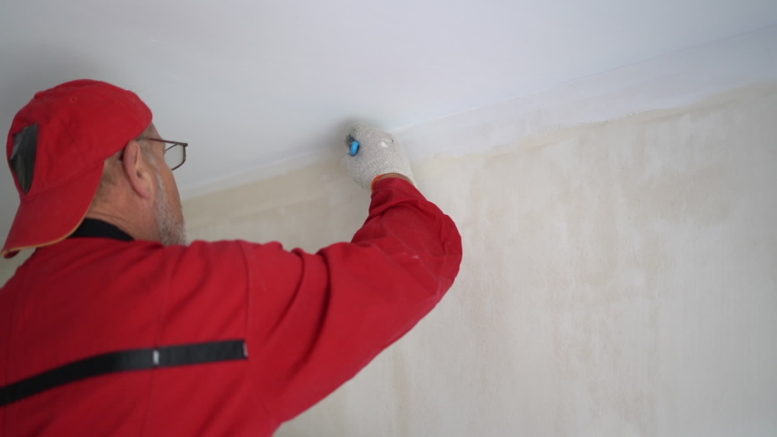 Renovation and interior decoration of a new house. A worker in red overalls paints the ceiling with white paint
