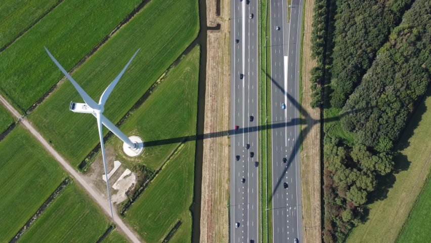 Aerial top down view of wind turbine and highway with traffic moving both ways turbines creating electricity in eco-friendly way for sustainable renewable powering vehicles 4k high resolution | Shutterstock HD Video #1081973747