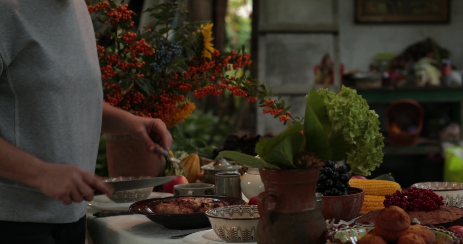 Woman cut stuffed turkey roll using knife and two prong fork on Thanksgiving dinner table with vintage crockery and autumn floral arrangement. Traditional Thanksgiving turkey roulade roasted on grill