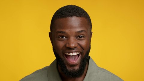 Excitement Concept. Portrait Of Happy Excited Black Man Opnenin Mouth In Amazement While Looking At Camera, Emotional African American Man Posing Over Yellow Studio Background, Slow Motion Footage