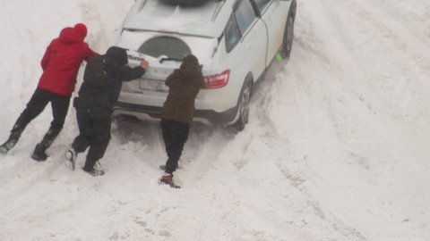 people push out a passenger car that stalled in the snow in winter, wheelspin