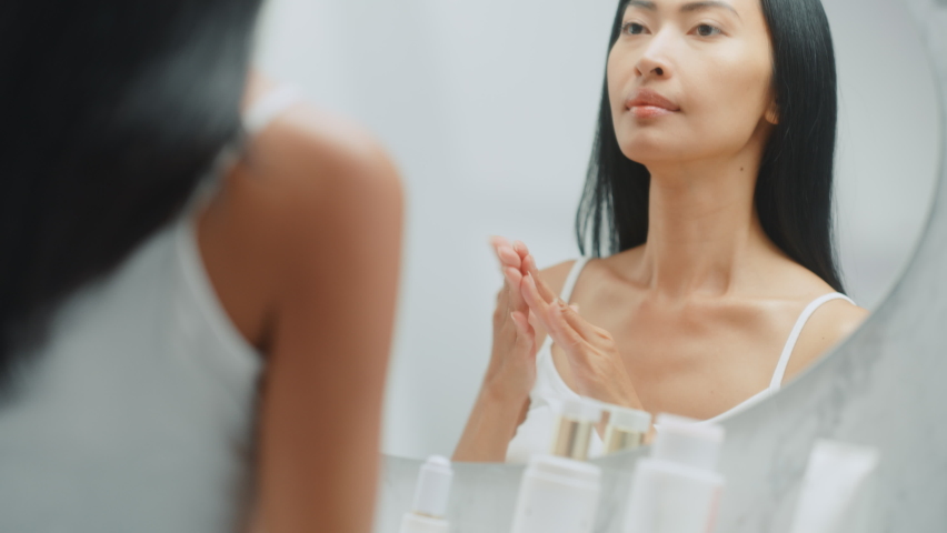 Beautiful Asian Woman Her Perfect Soft Face Skin, Uses Advanced Organic Cream, Smiles in the Mirror. Happy Female Enjoying Her Morning Beauty Routine. Wellbeing, Natural Beauty, Cosmetic Products | Shutterstock HD Video #1081983998