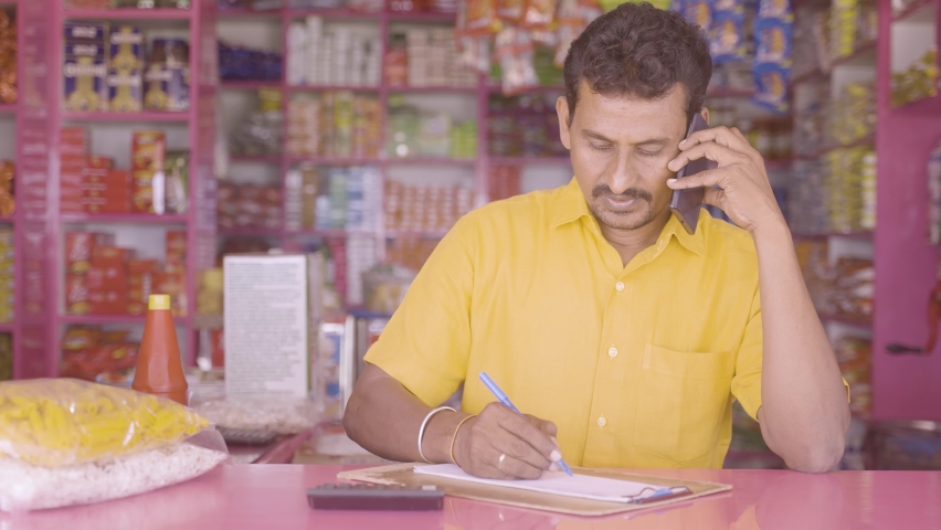 Kirana merchant or owner taking orders by noting from customer over Mobile phone call at groceries shop - concept of small business and Home delivery services | Shutterstock HD Video #1081985156
