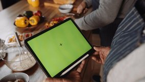 Birds eye view of Multi-cultural elderly couple cooking in kitchen referring to recipe on electronic tablet - Powered by Shutterstock - Get 15% off with code: PIKWIZARD15