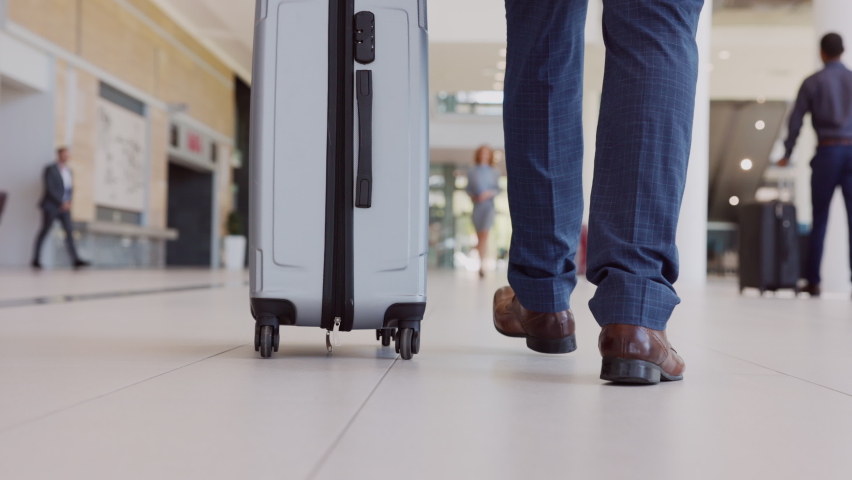 Low angle view of a passenger walking with his trolley in airport. Business man pulling his luggage in airport terminal with other people in background. Walking in a terminal before catching a flight. Royalty-Free Stock Footage #1081987019