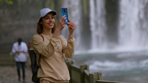 attractive smiling woman tourist making selfie on mobile phone on Lower Duden Waterfall background in Antalya. Famous view point and touristic place in Turkey.