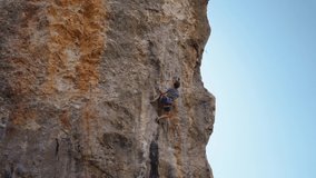 strong and skillful man climber climbs on vertical limewall crag by challenging route, makes hard effort and grabs hold. extreme sport and healthy lifestyle