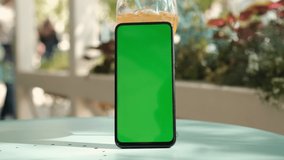 smartphone with mockup green screen standing on a table in a cafe