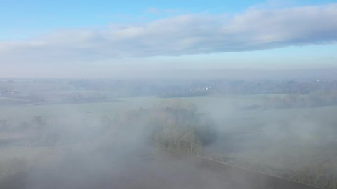 The morning fog over fields and a village in Europe, in France, in the Center region, in the Loiret, towards Orleans, in Winter, on a sunny day.