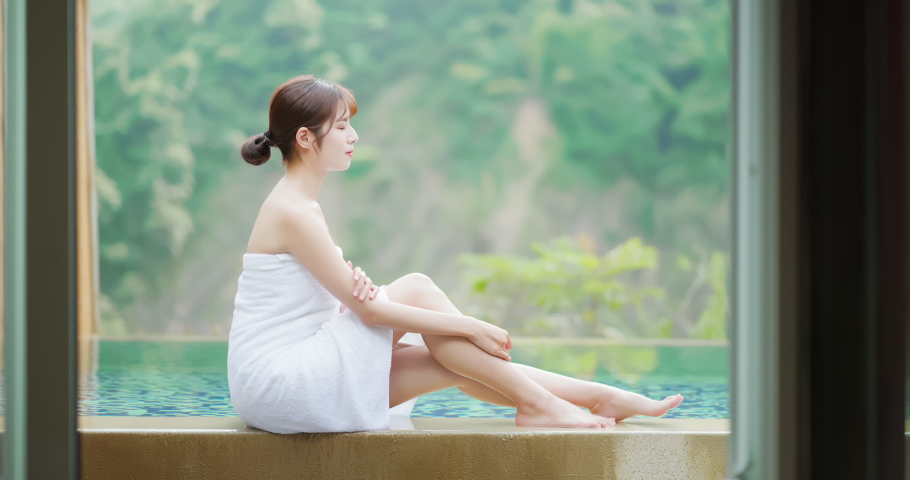 asian woman sitting by hot spring pool feel relaxing and touch her legs