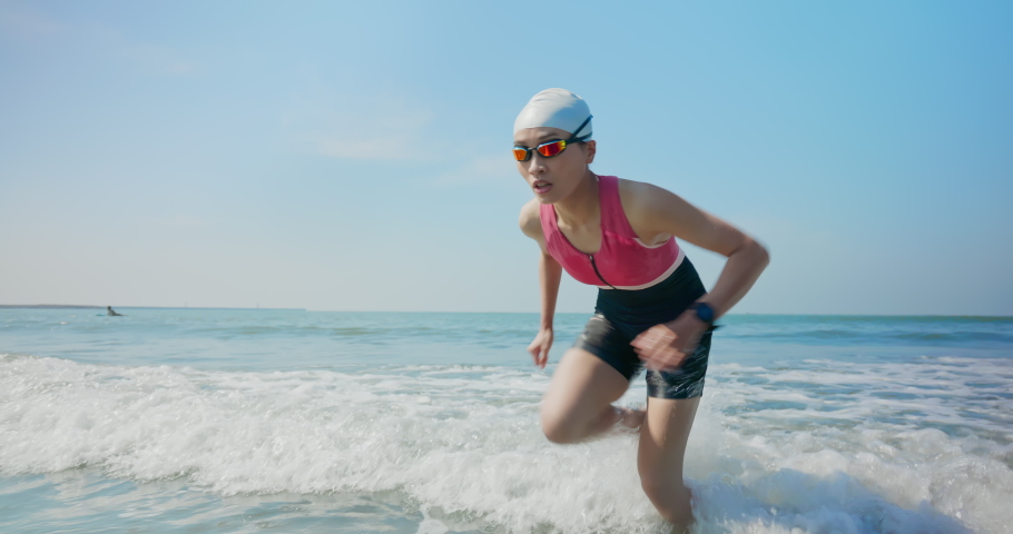asian woman wearing swimming goggles is running in water training for triathlon at beach