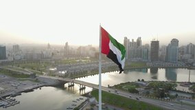 The Flag of the United Arab Emirates waving in the air, the Blue sky and city development in the Background, The national symbol of UAE over Sharjah's Flag Island. 4k Footage - Powered by Shutterstock - Get 15% off with code: PIKWIZARD15