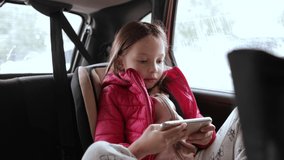 a little girl is playing on a smartphone sitting in a child seat in a car
