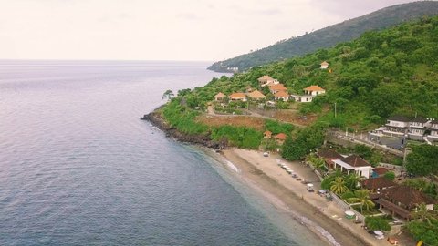 Drone flight over scenic landscape and cliffside tropical resort on summer day. Villas, pools, seaside resort, coastal road and mountains covered with lush from above. Travel, summer and tourism