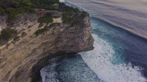 Amazing aerial view of curvy cliffside coastal beach with big sea foaming waves crashing on the shore. Beautiful nature landscape in tropical island.