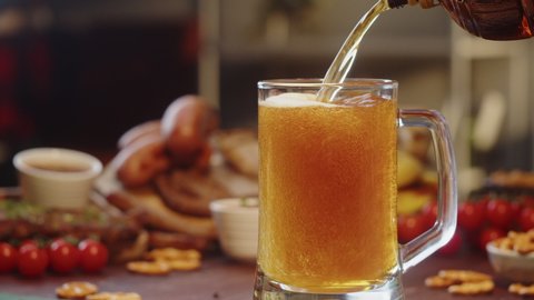 Pouring beer in glass close-up. Cafe restaurant with european gastronomy food. Traditional czech or german cuisine. Fried sausages, bratwursts on background. 
