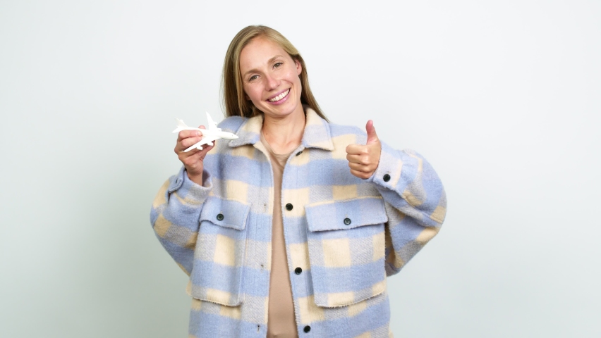 Young blonde girl holding a toy airplane and with thumb up over isolated background