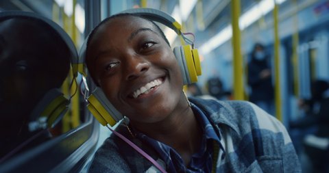 Cinematic close up of young african woman listening to music with headphones and looking through window while travel by train at night. Concept: transportation,technology, dreams, tourism, inspiration