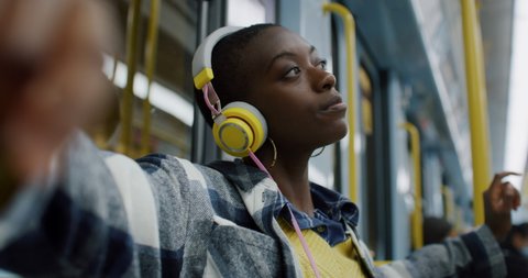 Cinematic shot of young african woman with headphones listening to music and dancing while traveling by train in subway. Concept of entertainment, transportation, technology, tourism, inspiration.
