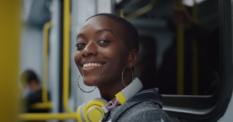 Cinematic shot of young african woman with headphones relaxing by listening to music while traveling by train in subway. Concept of entertainment, transportation, technology, tourism, inspiration.