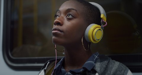 Cinematic shot of young african woman putting on headphones for listen her favorite music while traveling by train in subway. Concept of entertainment, transportation, technology, tourism, inspiration