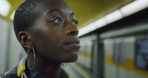 Cinematic close up of young african woman is waiting for train at subway station with passing train. Concept of transportation, travel, urban, lifestyle, tourism, traveling, city life, monopolies.
