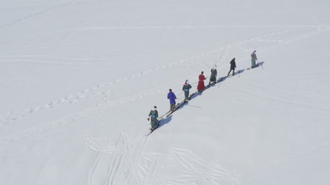 Skiers in traditional Tuva robes walking on fur skis in snow, aerial drone view winter