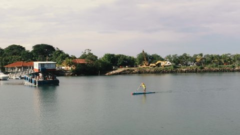 A paddleboarder hastily paddling past the font of a barge on his morning exercise routine, the vessel captain heading out to start his morning shift and collect his first load of cargo, Panama City