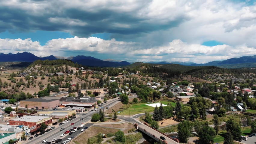 Aerial: Downtown of Pagosa springs in Colorado during cloudy day and mountain range in background - Cars driving on rural road of small village town in America